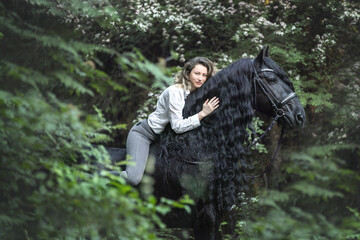 Beautiful young lady posing with a purebred friasian horse in the forest. - 459062628