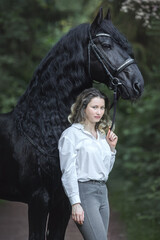 Beautiful young lady posing with a purebred friasian horse in the forest.