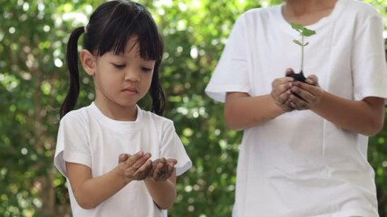 Asian kids with attractive age 4 to 8 years, with a heart to love the world Growing seedlings from black soil concentrate Happy smiling face The background is a green tree. Earth Day concept