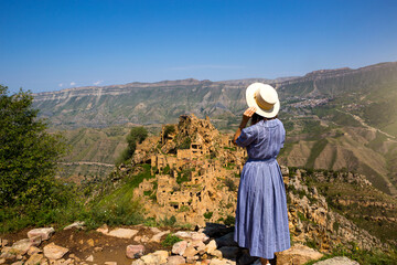 Fototapeta na wymiar Female tourist high in mountains of Dagestan admires the breathtaking panoramic view of nature and the ancient abandoned city of Gamsutl. Caucasus mountains, tourist attraction, ruins, trekking tour