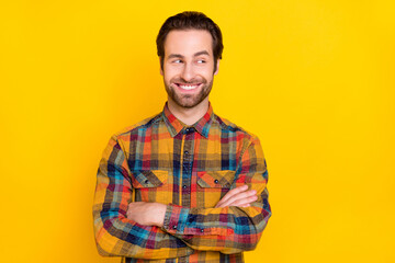 Photo of confident pretty young guy dressed checkered shirt arms crossed looking empty space smiling isolated yellow color background