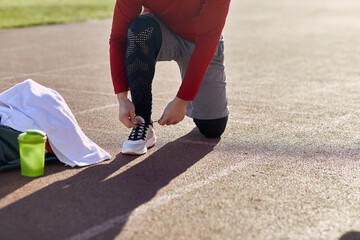 detail, cropped image of caucasian male kneeling on one knee at the stadium athletic track, tying...