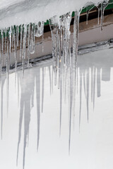 Icicles hang from the roof on a white wall and shine in sun