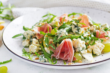 Salad of pear, blue cheese, grape, prosciutto, arugula and nuts with spicy dressing on a light background. Healthy eating.