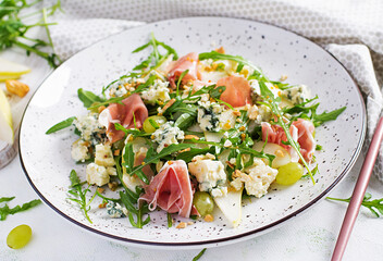 Salad of pear, blue cheese, grape, prosciutto, arugula and nuts with spicy dressing on a light background. Healthy eating.