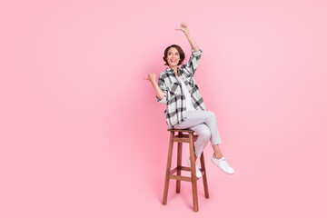 Full body photo of young woman happy positive sit chair point thumb empty space ad promo isolated over pink color background