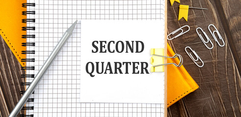 SECOND QUARTER text on a sticker on the notebook, wooden background