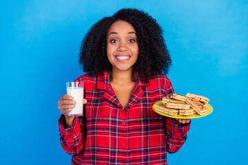 Photo of optimistic millennial brunette lady eat sweets drink milk wear red checkered sleepwear...