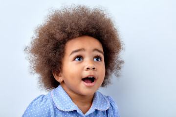 close-up portrait of cute surprised african child girl in blue t-shirt looking up at something...