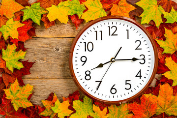 Colored autumn leaves and wall clock on wood background