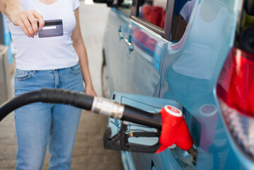 A woman fills her car with gasoline at a self-service gas station and holds a credit card