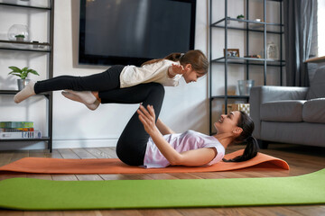 Happy sporty mom and daughter train together at home