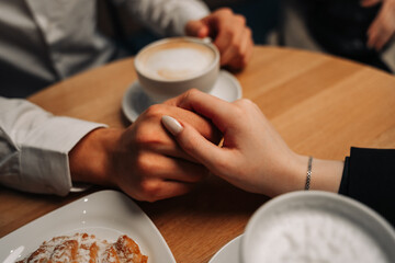 Romantic couple man and woman hold each other's hands in a cafe. There are pastries and coffee on the table.