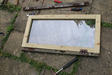 Close up of home made greenhouse window in glass and wood with hinge ready for staining, the renovated oblong pine wooden frame laid on patio outdoors on garden stone patio