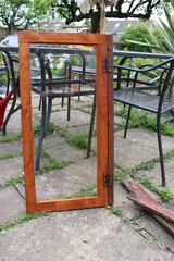Close up of home made carpentry greenhouse window in glass and stained wood, the renovated oblong pine wooden frame stood patio outdoors garden with metal furniture background
