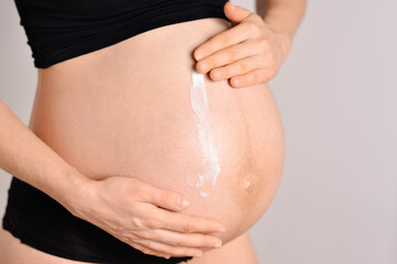 Pregnant woman applying cream at her belly for prevention of stretch marks on the skin in light...