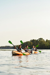 Sportive young friends paddling together on a river, spending weekend outdoors on a summer day