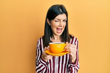 Young hispanic woman drinking a cup of coffee winking looking at the camera with sexy expression, cheerful and happy face.