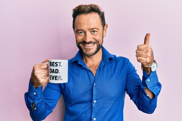 Middle age man drinking mug of coffee with best dad ever message smiling happy and positive, thumb up doing excellent and approval sign
