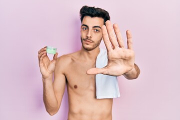 Fototapeta premium Young hispanic man shirtless wearing towel and eye bags patches with open hand doing stop sign with serious and confident expression, defense gesture