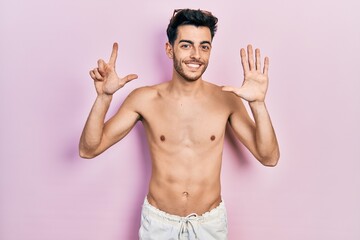 Young hispanic man wearing swimwear shirtless showing and pointing up with fingers number seven while smiling confident and happy.