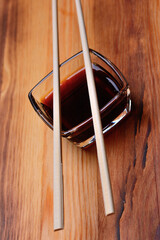 Soy sauce in a square glass bowl with chopsticks. On the background of a wooden texture
