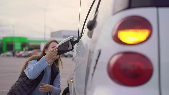 Broken off side rearview mirror on car. Woman is checking for damage on her auto