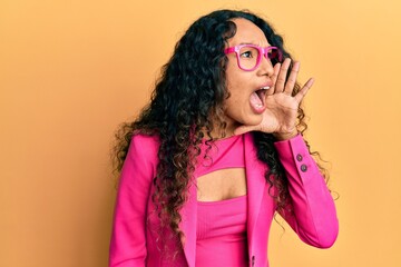 Young latin woman wearing business style and glasses shouting and screaming loud to side with hand on mouth. communication concept.