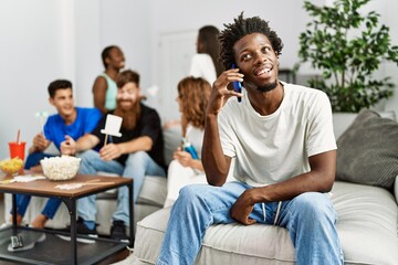 Group of young friends smiling happy sitting on the sofa. Man talking by the smartphone at home.