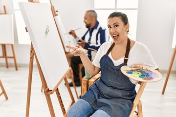 Young artist woman at art studio smiling happy pointing with hand and finger