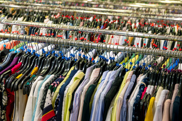 Bulk goods of different colored clothes are offered for sale in retail outlets. Shirts, blouses and vests on a clothes rack.