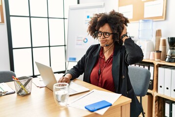 African american woman with afro hair working at the office wearing operator headset confuse and...
