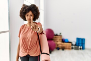 Fototapeta na wymiar African american woman with afro hair holding yoga mat at pilates room pointing with finger up and angry expression, showing no gesture