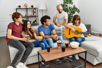 Group of young friends on party smiling happy and playing classical guitar at home.