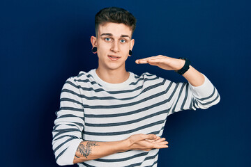Young caucasian boy with ears dilation wearing casual striped shirt gesturing with hands showing big and large size sign, measure symbol. smiling looking at the camera. measuring concept.