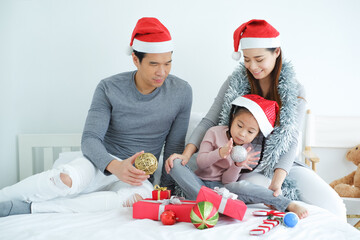 Asian family celebrating Christmas wearing red Santa Claus hat with decorative gifts and gift boxes or present in bedroom, holiday in festive Merry Christmas or X'mas and happy new year concept