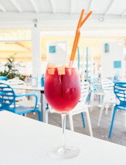 Spanish Sangria drink, made with red wine, sugar, liquor, apples and oranges, served in a crystal glass with two orange straws, on a summer terrace table in the Valencian Community, Spain.