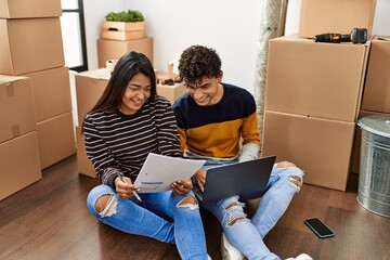 Young latin couple using laptop sitting on the floor at new home.