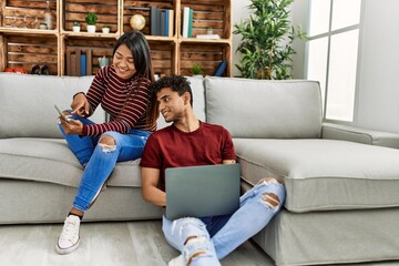Obraz premium Young latin couple smiling happy using laptop and smartphone at home.