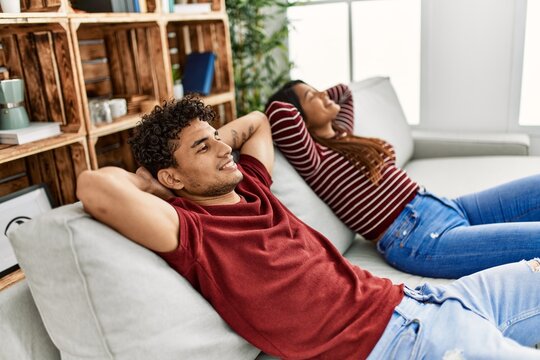 Young latin couple smiling happy relaxed with hands on head sitting on the sofa at home.