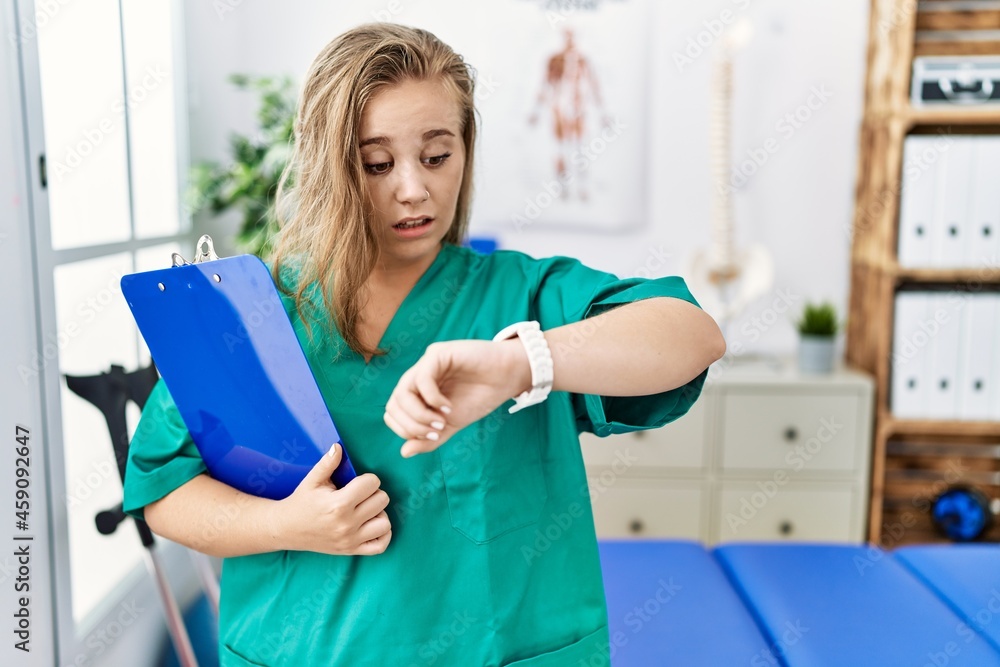 Sticker young caucasian woman working at pain recovery clinic looking at the watch time worried, afraid of g