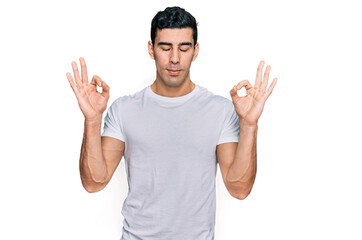 Handsome hispanic man wearing casual white t shirt relax and smiling with eyes closed doing meditation gesture with fingers. yoga concept.