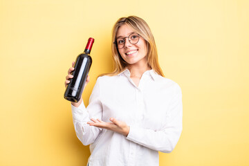pretty blonde girl smiling cheerfully, feeling happy and showing a concept. wine bottle concept - obrazy, fototapety, plakaty