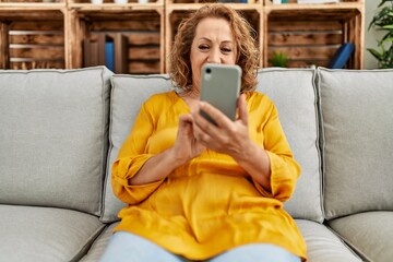 Obraz premium Middle age caucasian woman usin smartphone sitting on the sofa at home.