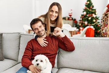 Young hispanic couple smiling happy sitting on the sofa with dog at home.