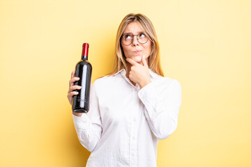 pretty blonde girl thinking, feeling doubtful and confused. wine bottle concept