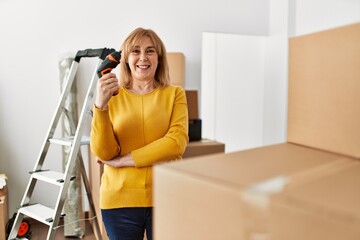 Fototapeta na wymiar Middle age blonde woman smiling happy using drill at new home.