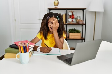 Young african american girl doing homework at home yawning tired covering half face, eye and mouth with hand. face hurts in pain.