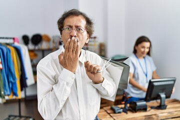 Southeast asian man wearing holding shopping bags covering mouth with hand, shocked and afraid for mistake. surprised expression
