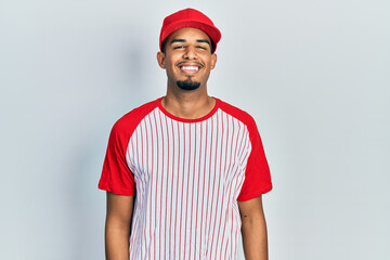 Young african american man wearing baseball uniform smiling and looking at the camera pointing with two hands and fingers to the side.